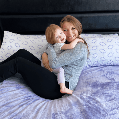 Woman and child sitting on a bed with patterned pillows and bedding

