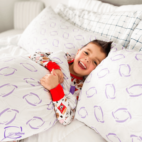 Child lying in bed with a Omnipillow, a pillow with purple oval patterns.

