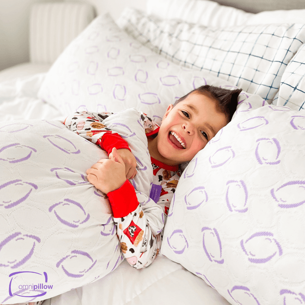 Child lying in bed with a Omnipillow, a pillow with purple oval patterns.


